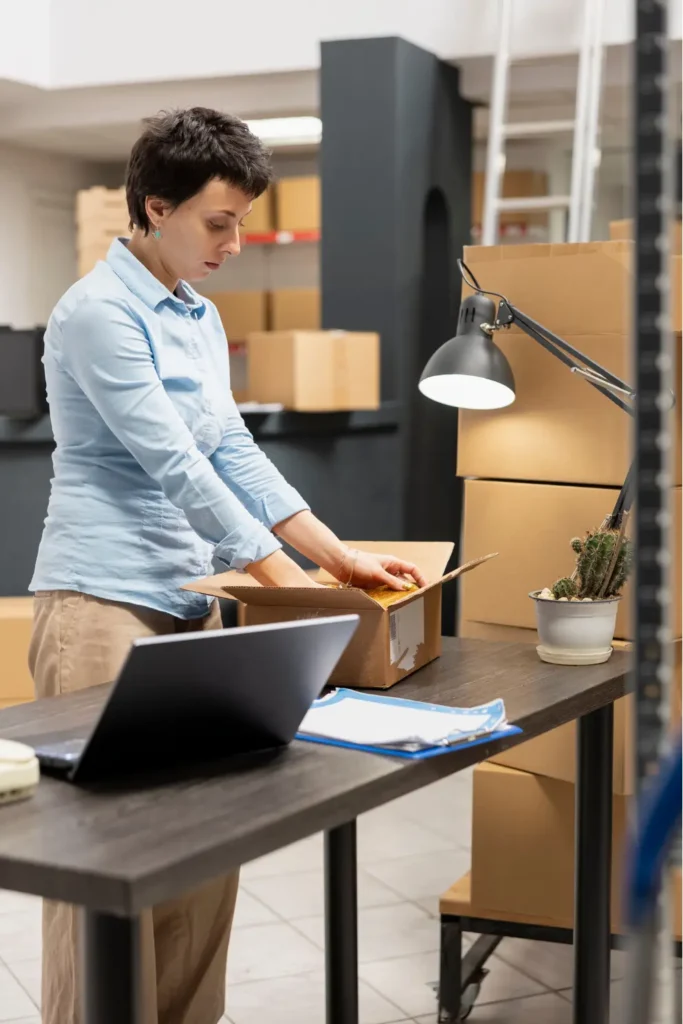 Removal company staff packing a box at a desk with a laptop in a storage workspace